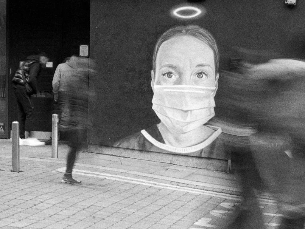 Blurred people walk past street art showing a masked nurse with a halo over her head