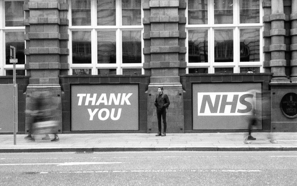 A man standing between large signs thanking the NHS while blurred people walk by