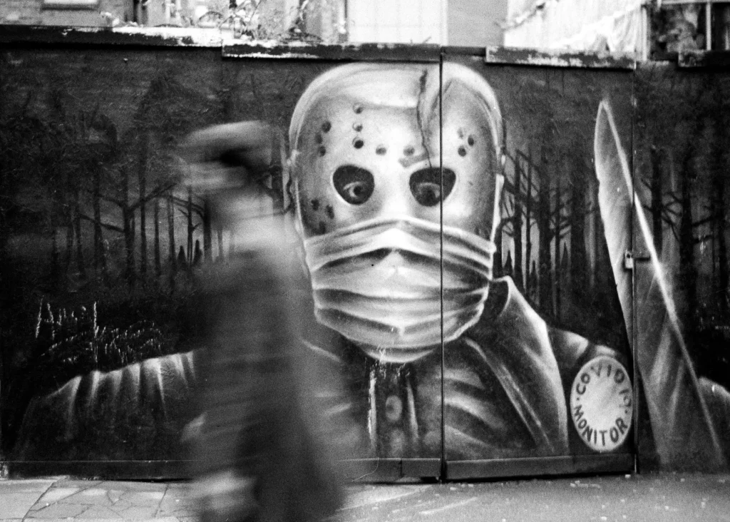 A blurred person walks past street art of a scary knife wielding Covid-19 monitor