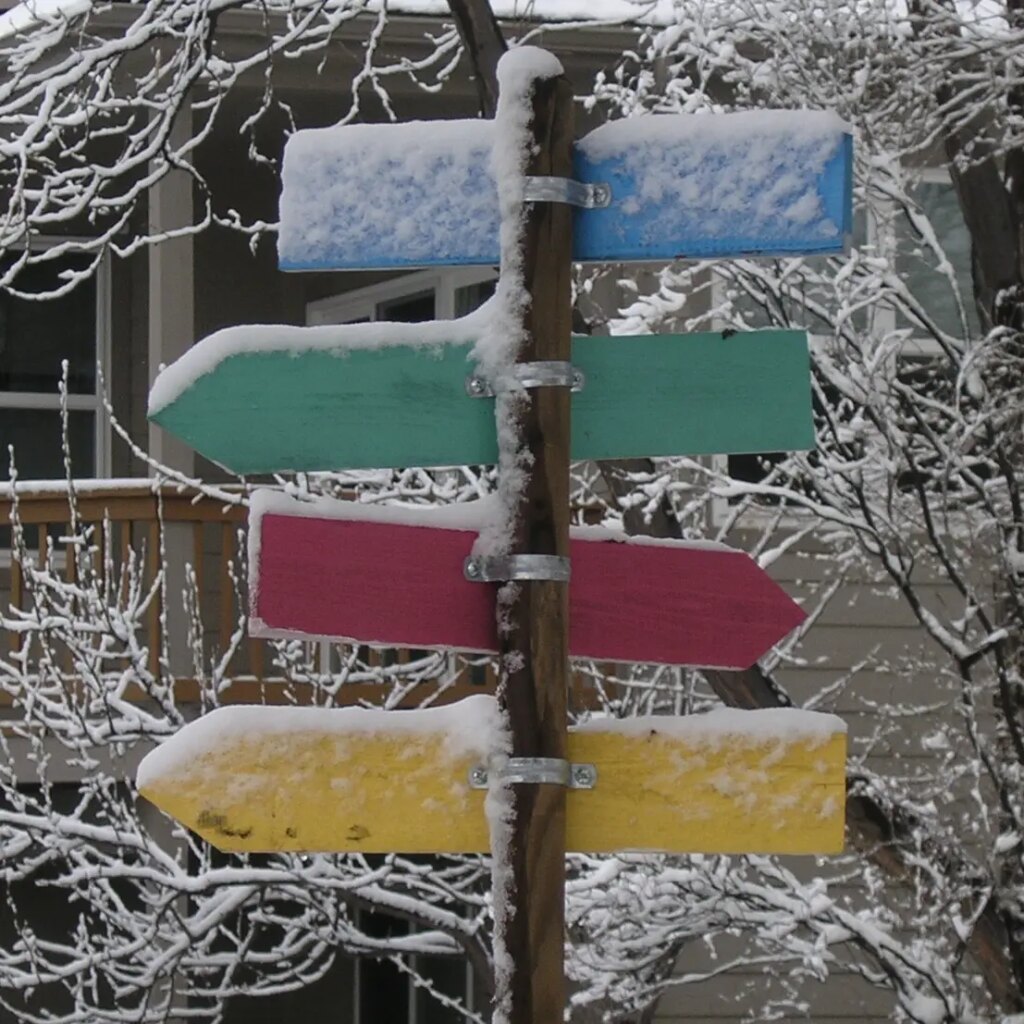 an arrow sign with four parts/four different colors pointing in two directions, no words, and a bit of snow