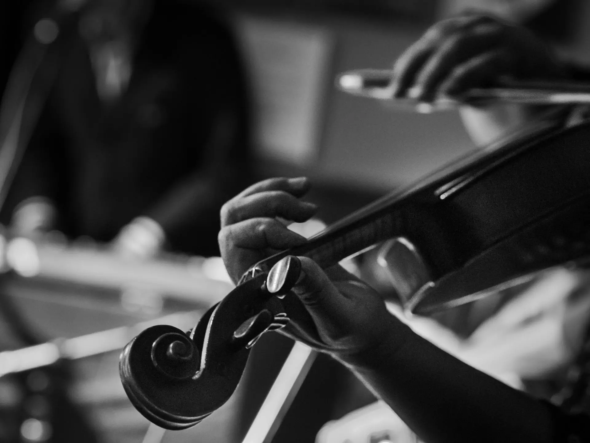 black and white close up image of a woman playing the violin, with a man playing piano in the background