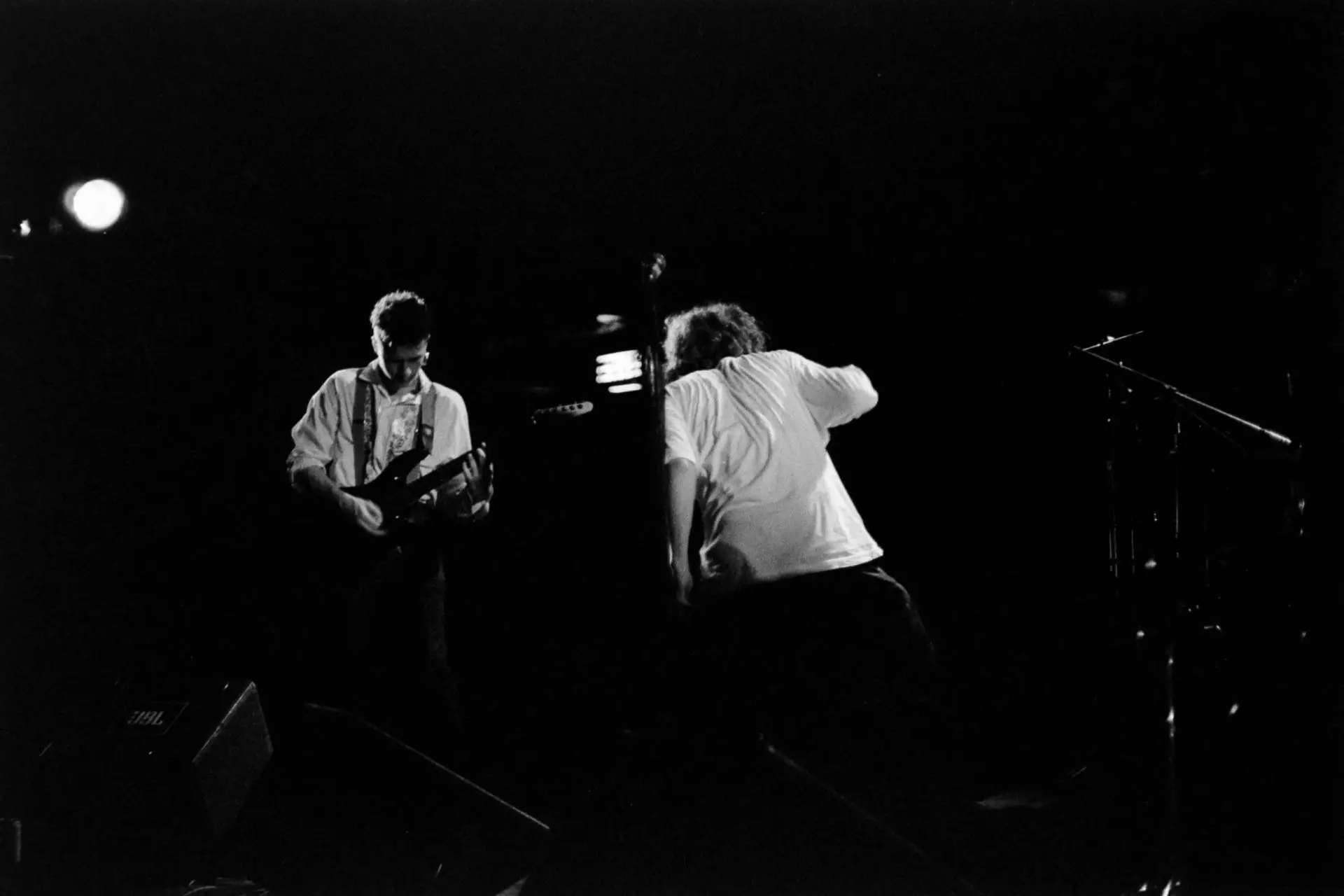 black and white image of a man singing, with a man playing the guitar in the background