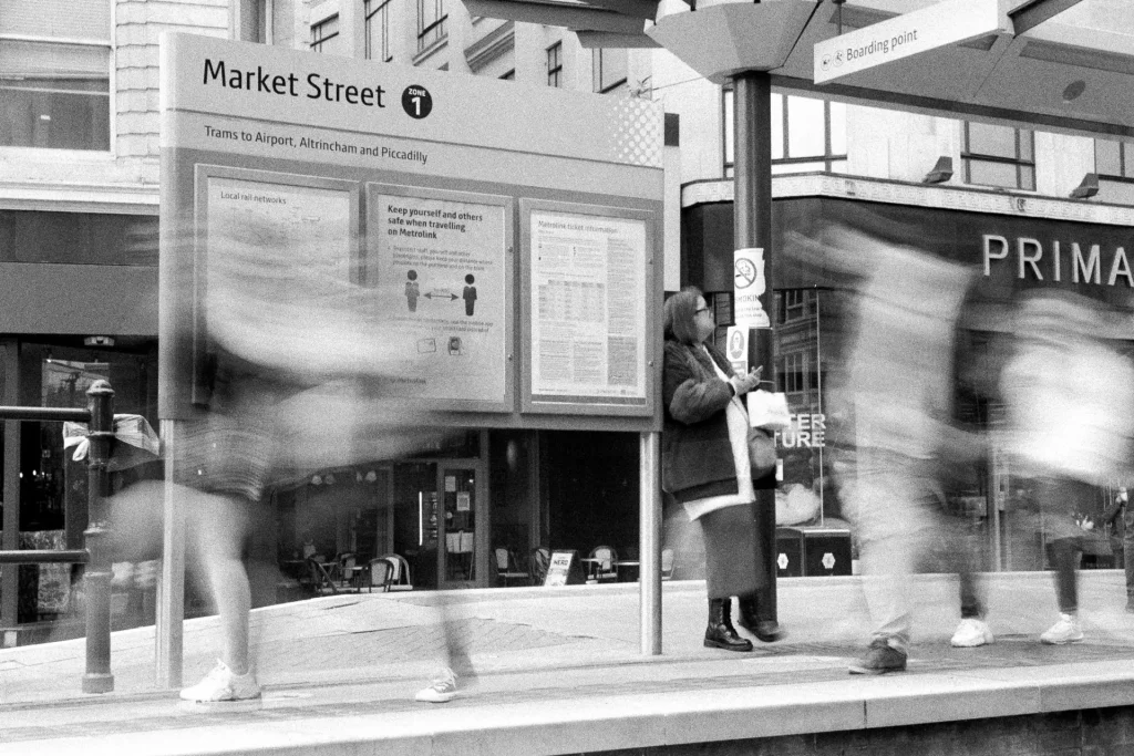 Blurred people walk past a lady waiting for a tram and a social distancing poster