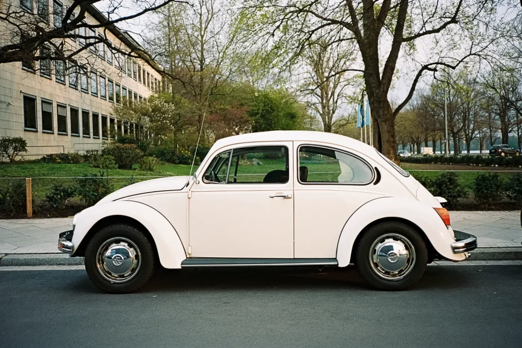 A white Volkswagen Beetle parked at the side of a road, captured with a point-and-shoot camera.