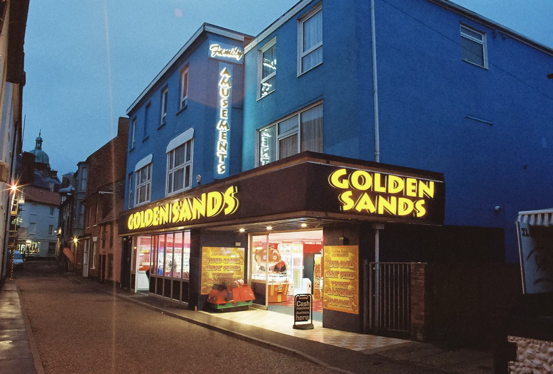 Illuminated yellow sign in the words Golden Sands along the front and down the side of the overhanging arcade front.