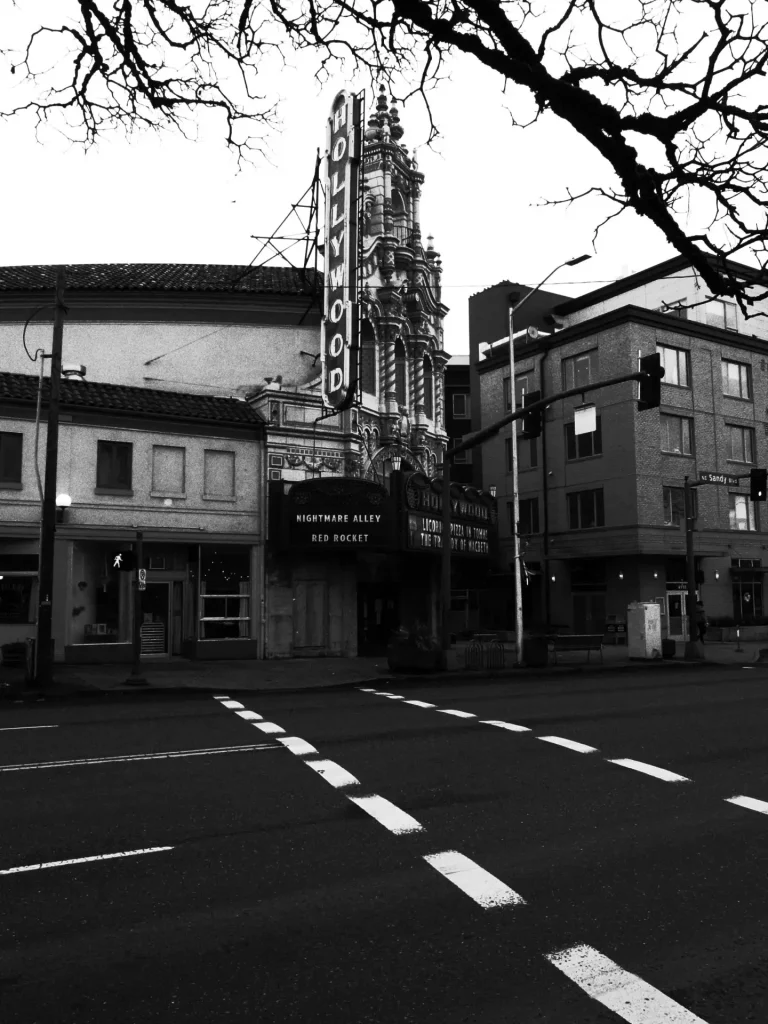 A black and white photo of the Hollywood Theater in Portland, Oregon with crosswalk lines stretching across the foreground. 