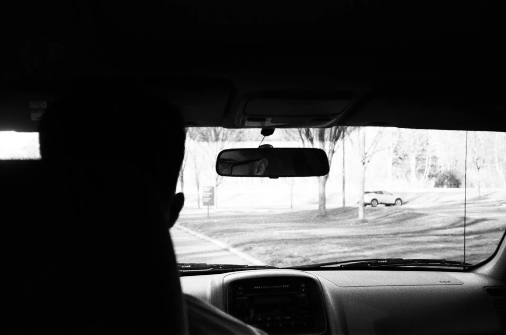 A silhouette of a man driving and his reflection in the rear view mirror