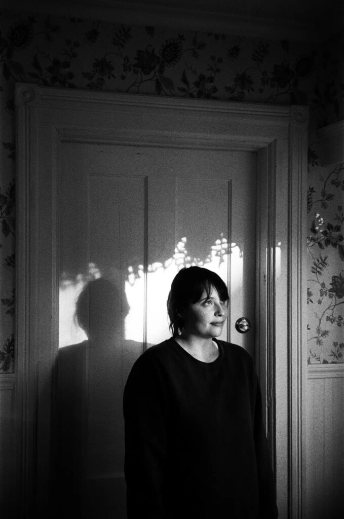A woman standing in a doorway with the shadows of curtains around her