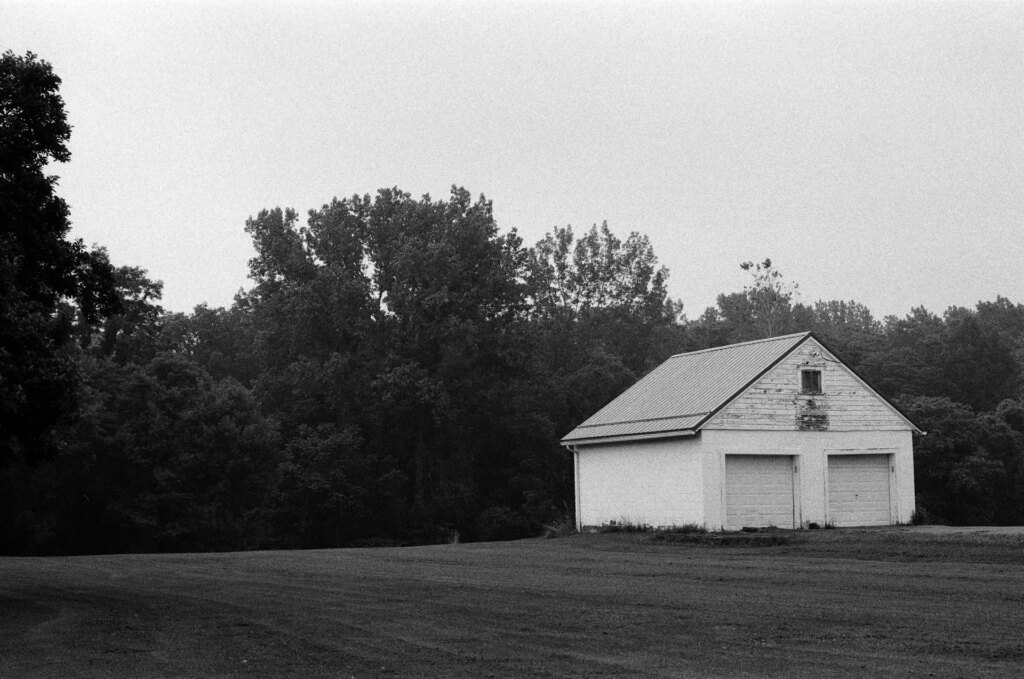 A barn in a lawn against a forest