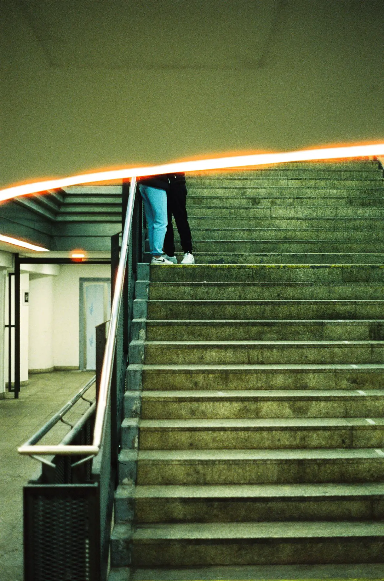 A couple standing in front of each other on stairs in a train station. you only see their legs.