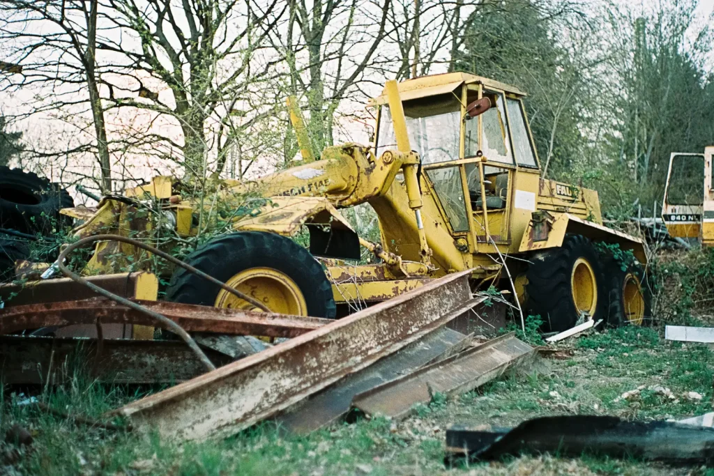 A decommissioned grinder is overgrown by bushes on the machine boneyard.