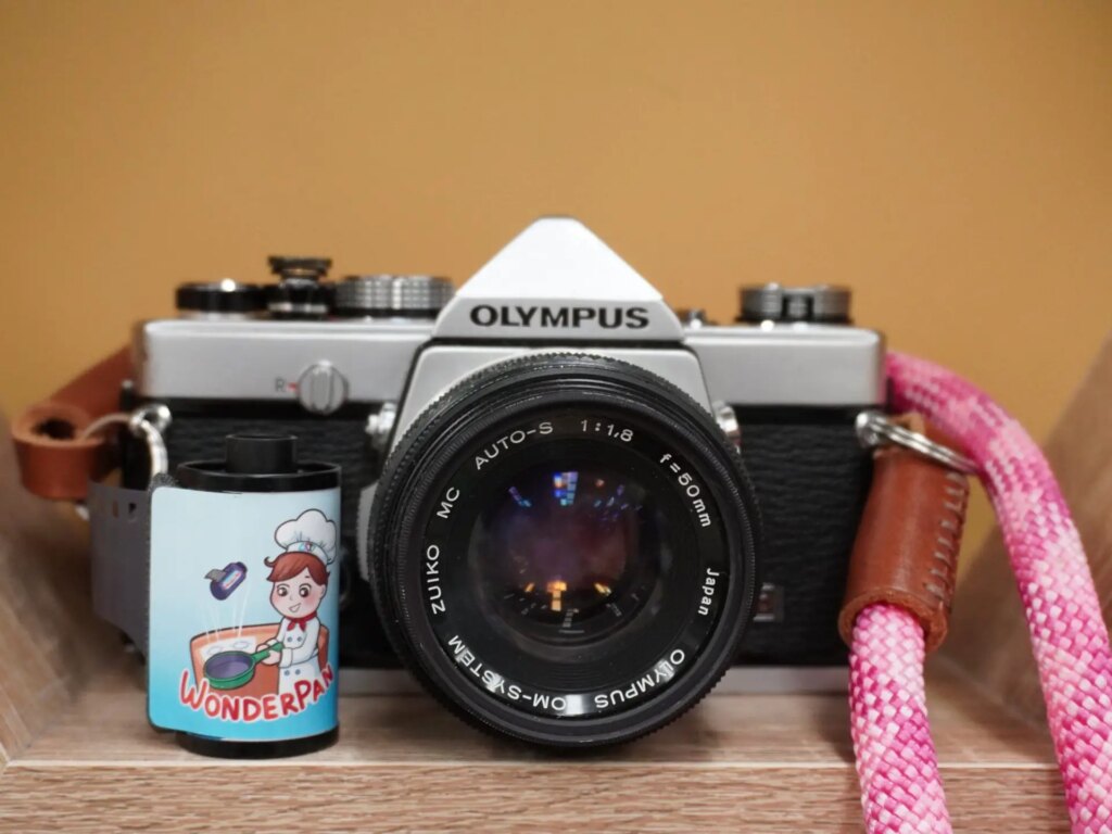 lifestyle product shot of wonderpan 400 film roll sitting next to film camera with pink straps