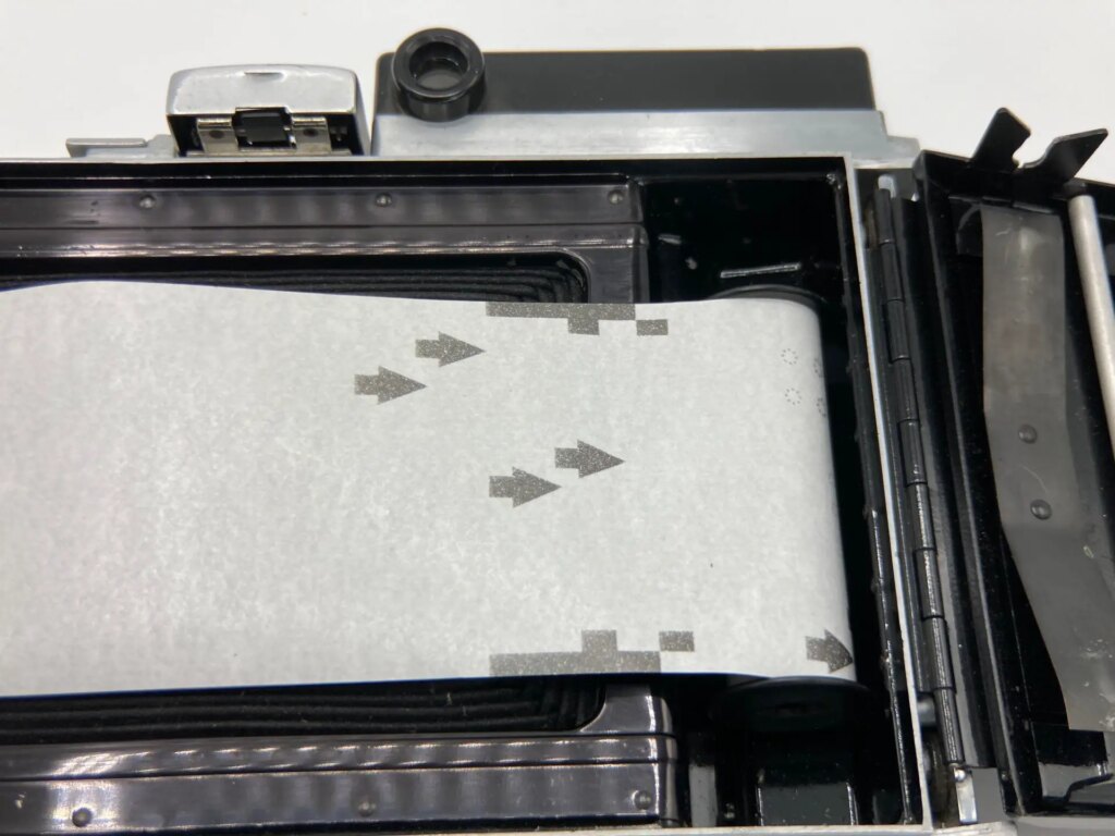 120 medium format film backing paper laid into a Polaroid Pathfinder 110 camera to demonstrate how film travels