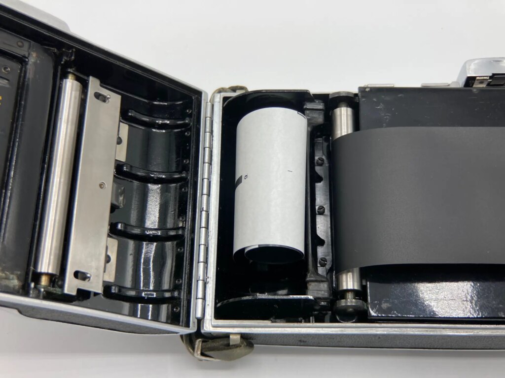 120 medium format film backing paper laid into a Polaroid Pathfinder 110 camera to demonstrate how film travels