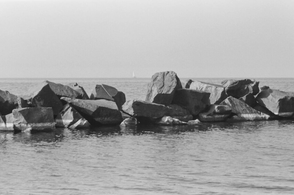 Lake view with a stone breakwater and a sail boat on the horizon