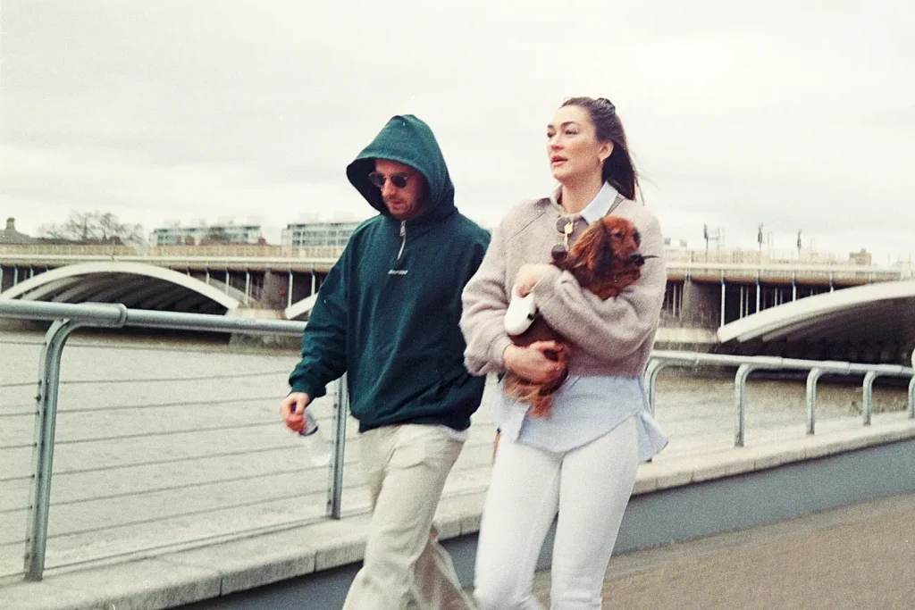 Couple walking and woman carrying a brown dog along the Thames river