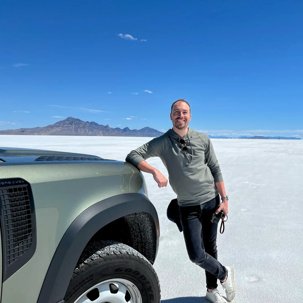 Kyle from Grainery leaning on the edge of a car in the desert with white sands and blue skies