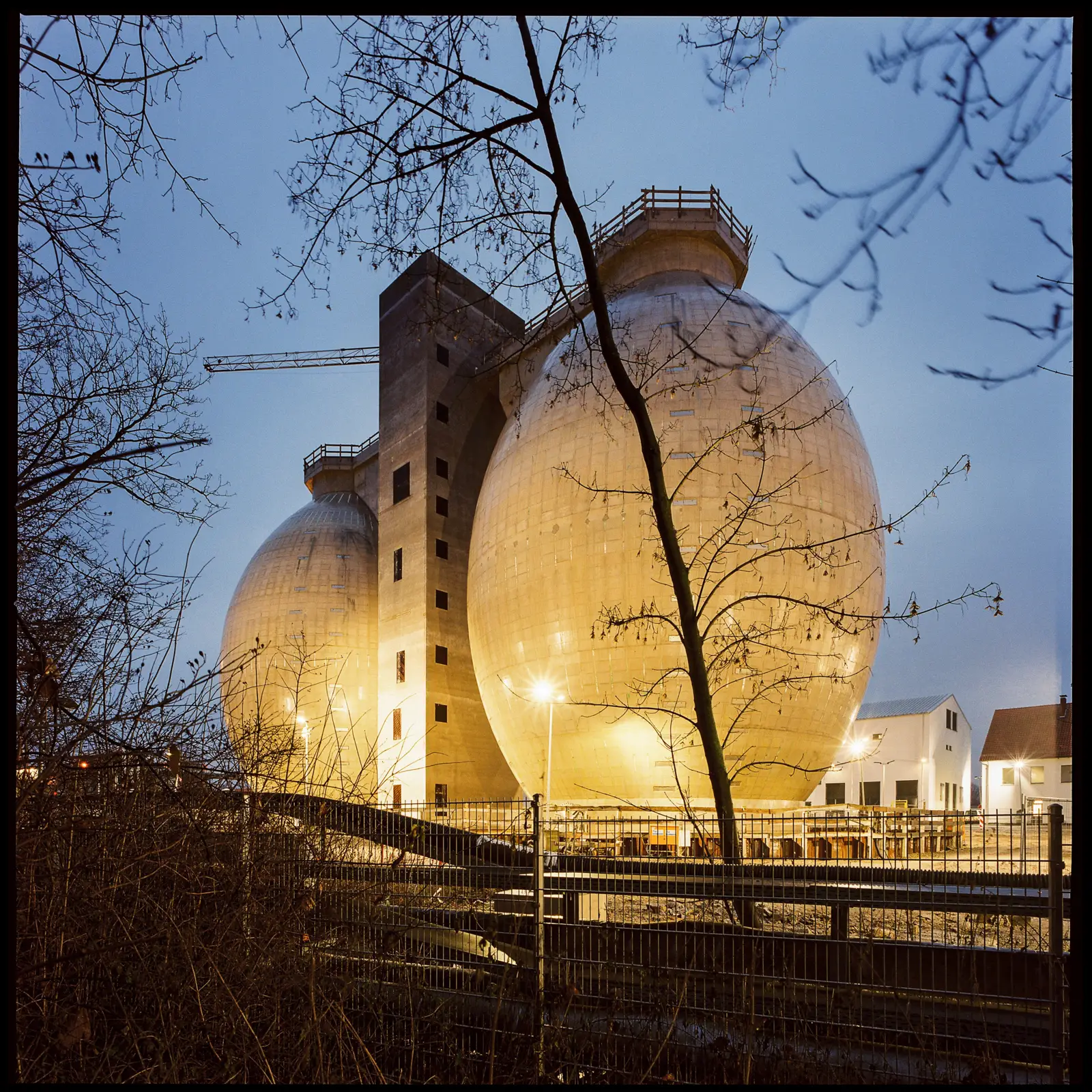 two egg-shaped concrete towers in front of an evening sky, lit by several spotlights and with lots of tree branches in the foreground