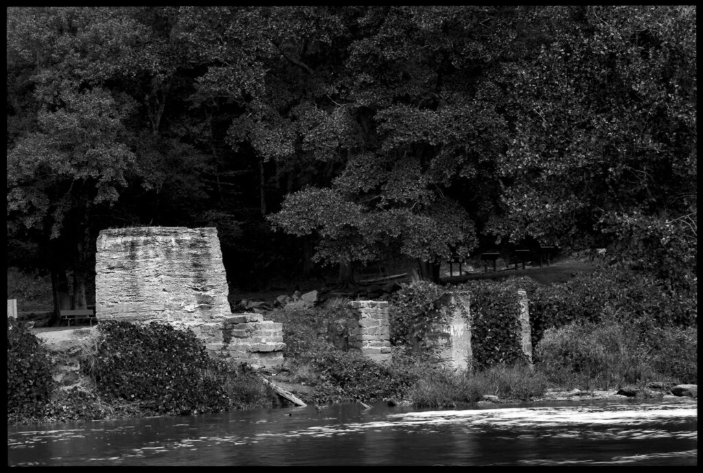 A river flow along a bank built up along concrete, stone and brick ruins.