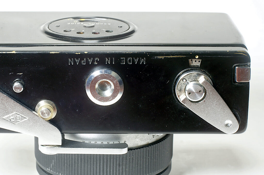 Rewind crank with small button at 11 o'clock that engages clutch for rewinding. Button at left to disengage film wind.