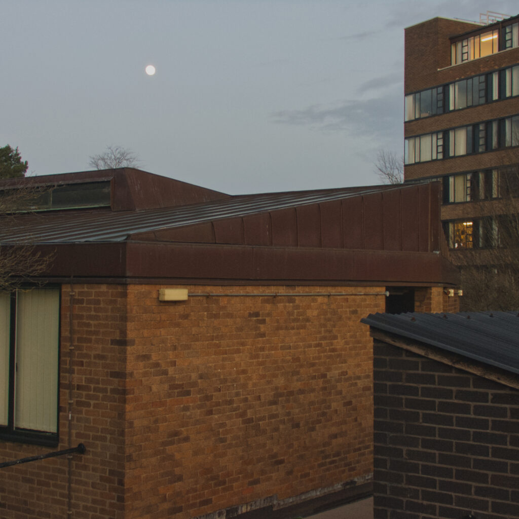 Picture of buildings with a very small moon in the distance. 