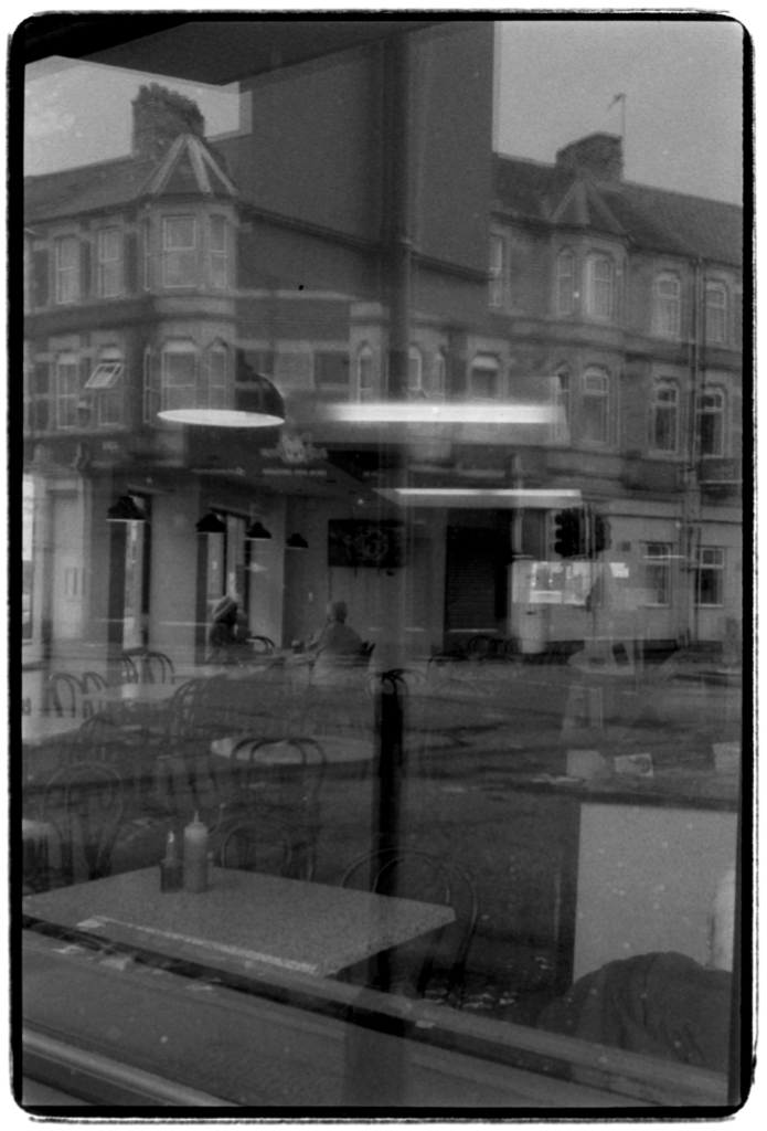 Two people sat in a cafe intermingled with reflections of the building across the road.