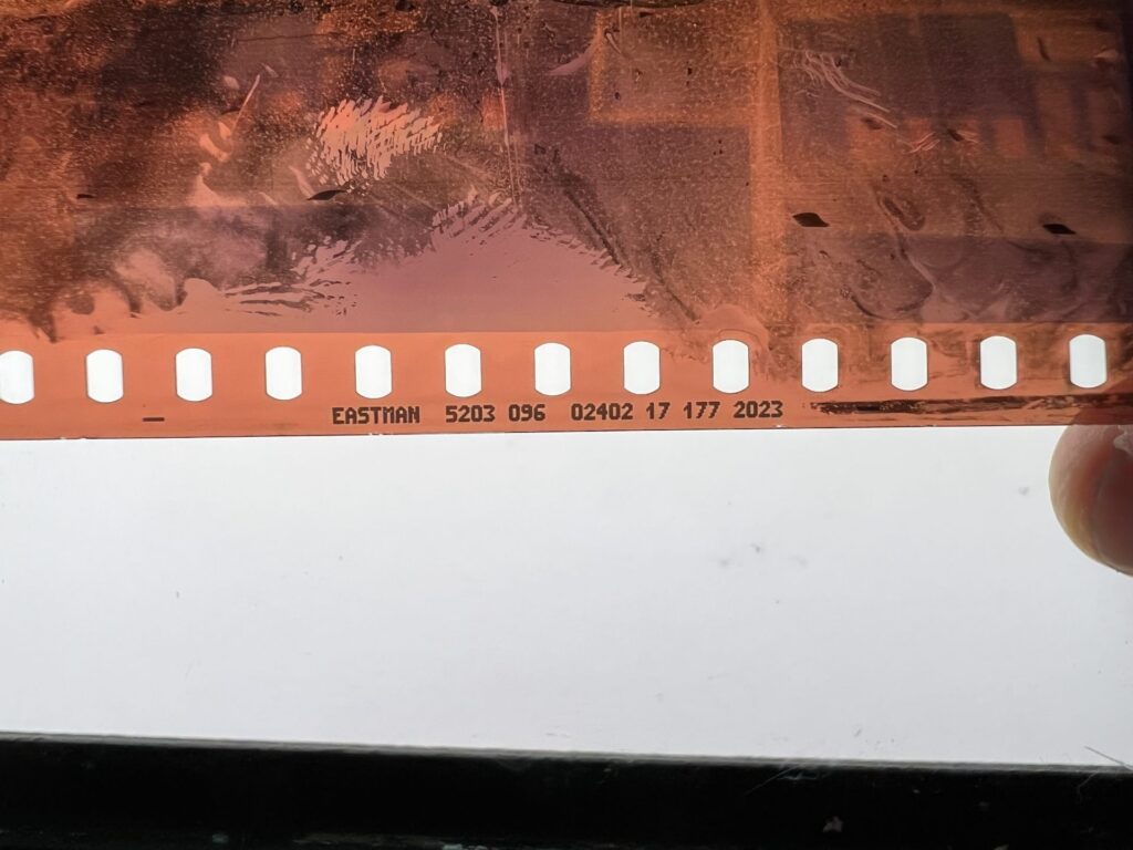 a closeup photo of the edge of a 35mm film strip on a light table, showing the sprocket holes and edge marking. 