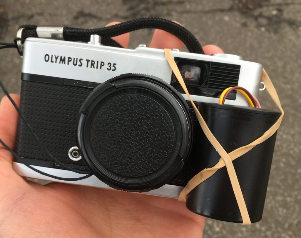 A hand holding a modified Olympus Trip 35 camera.