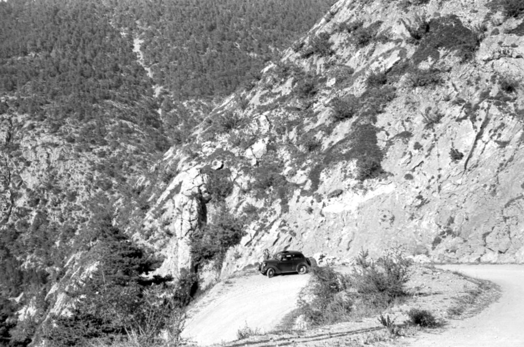 Black and white image of a car parked on a hairpin bend.