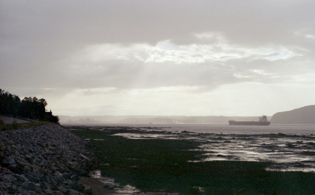 Sunlight shining through clouds over bay with ferryboat in the distance