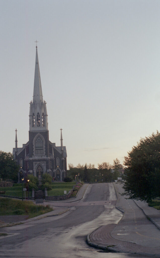 Church with tower next to road, surrounded by greenery