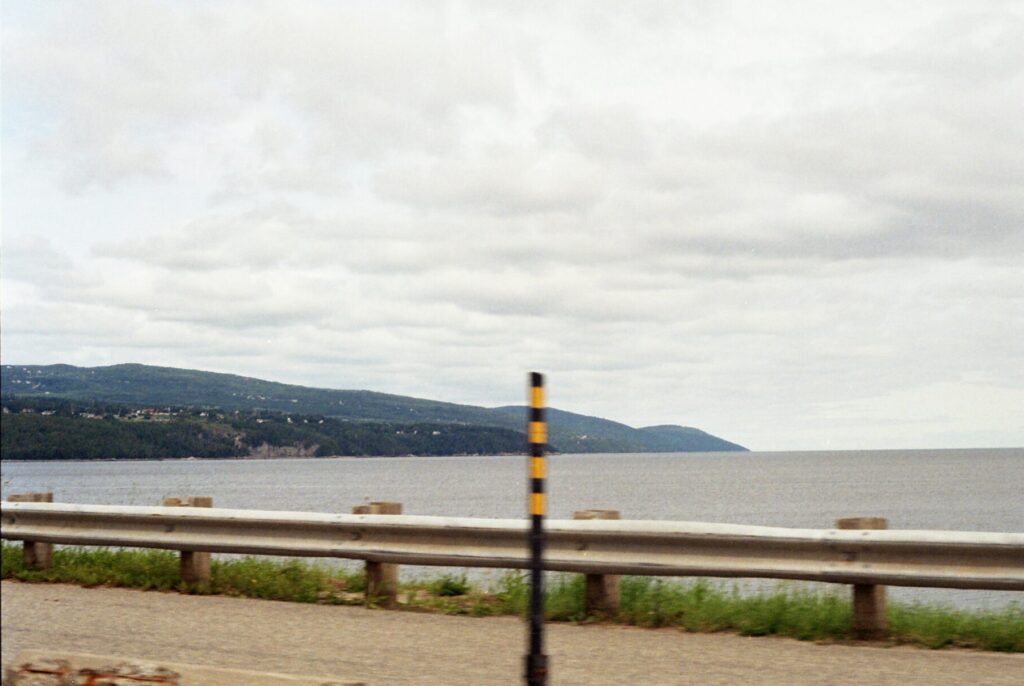 Bank of river from the road with the railing visible, traffic post breaking the horizon