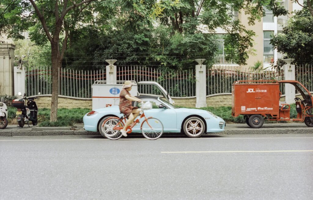 An older chinese lady cycles past a Porsche. i'm more a fan of her bicycle than I am the expensive sports car.