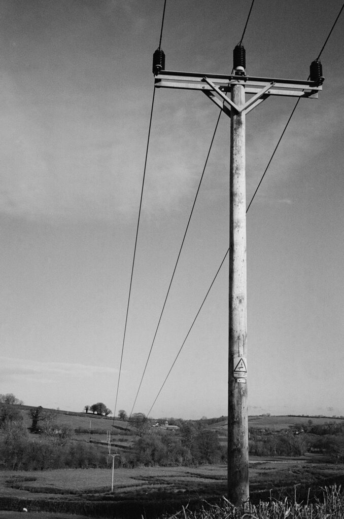 Black and white photo of a telegraph pole with cables stretching into the distance over fields.