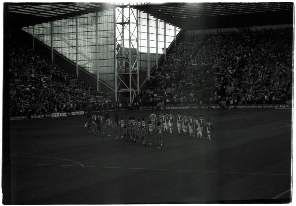 Liverpool FC and Darmstadt 98 walk out onto the pitch at Deepdale as fans hold scarves aloft. Shot on Rollei Retro 400s with Pentax Espio 170SL