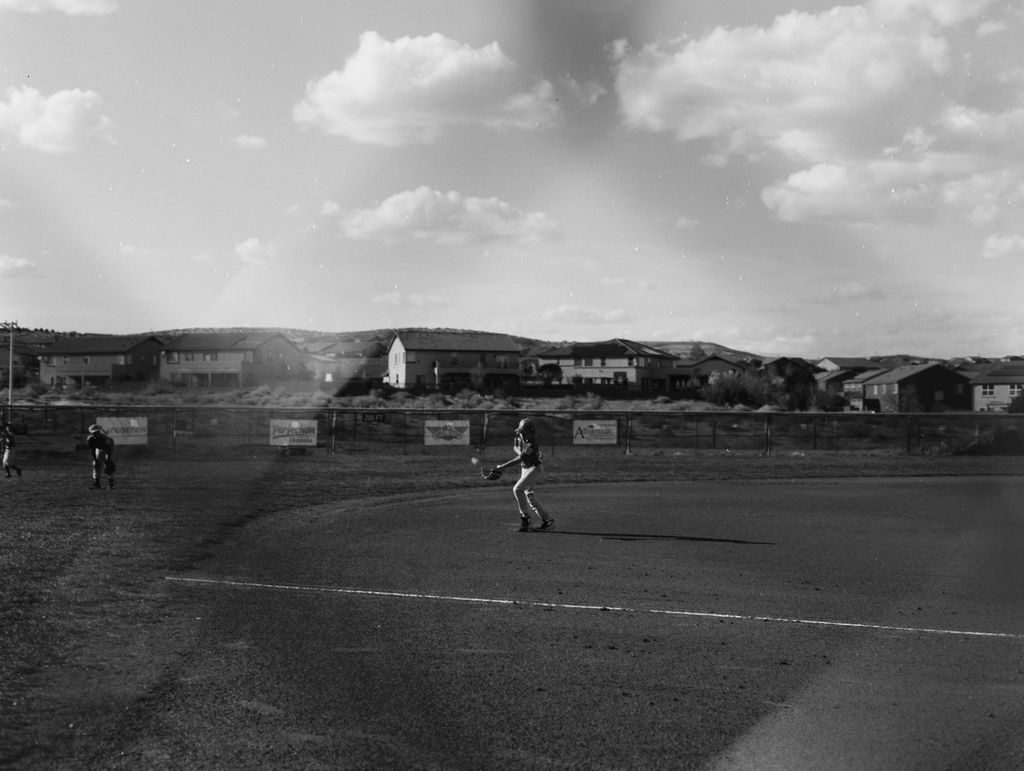Image of kids playing a baseball game with a view through the chainlink fence.