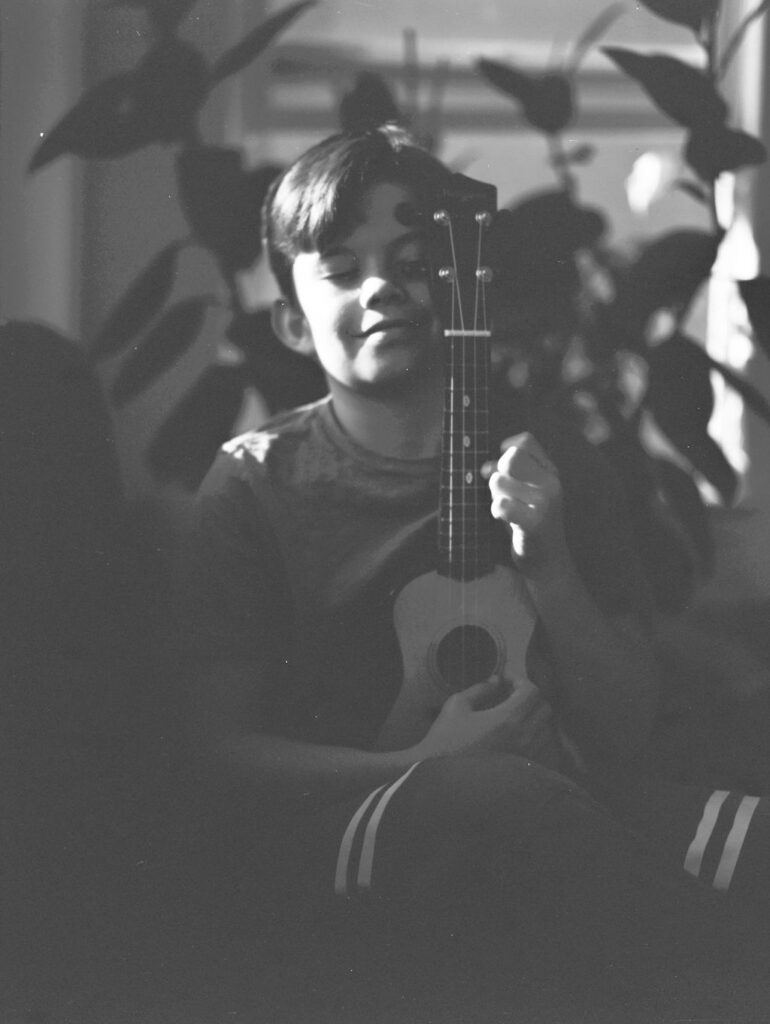 A young boy with his eyes closed and a ukulele against his chest.