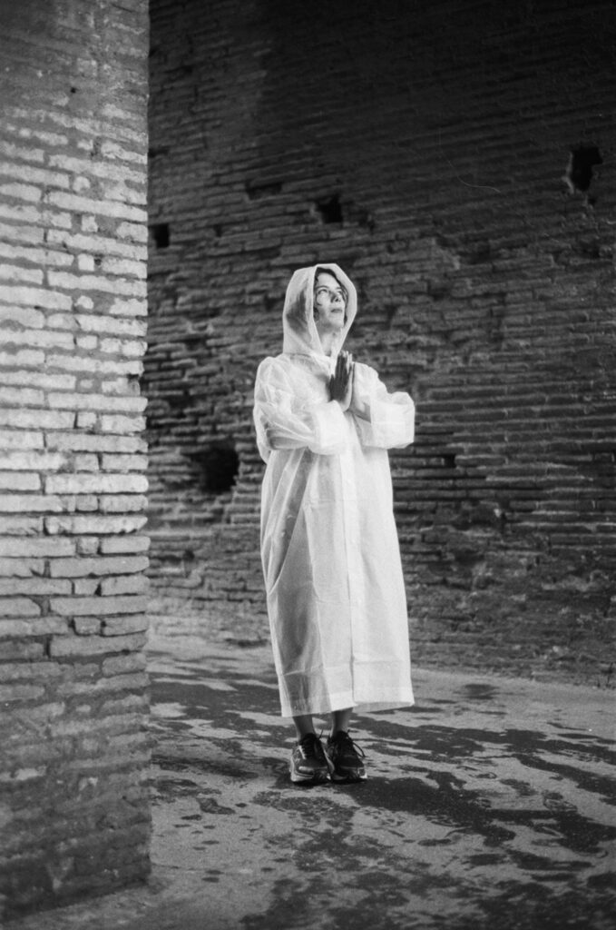 a woman wearing a raincoat standing in a brick arch with her hands in a prayer