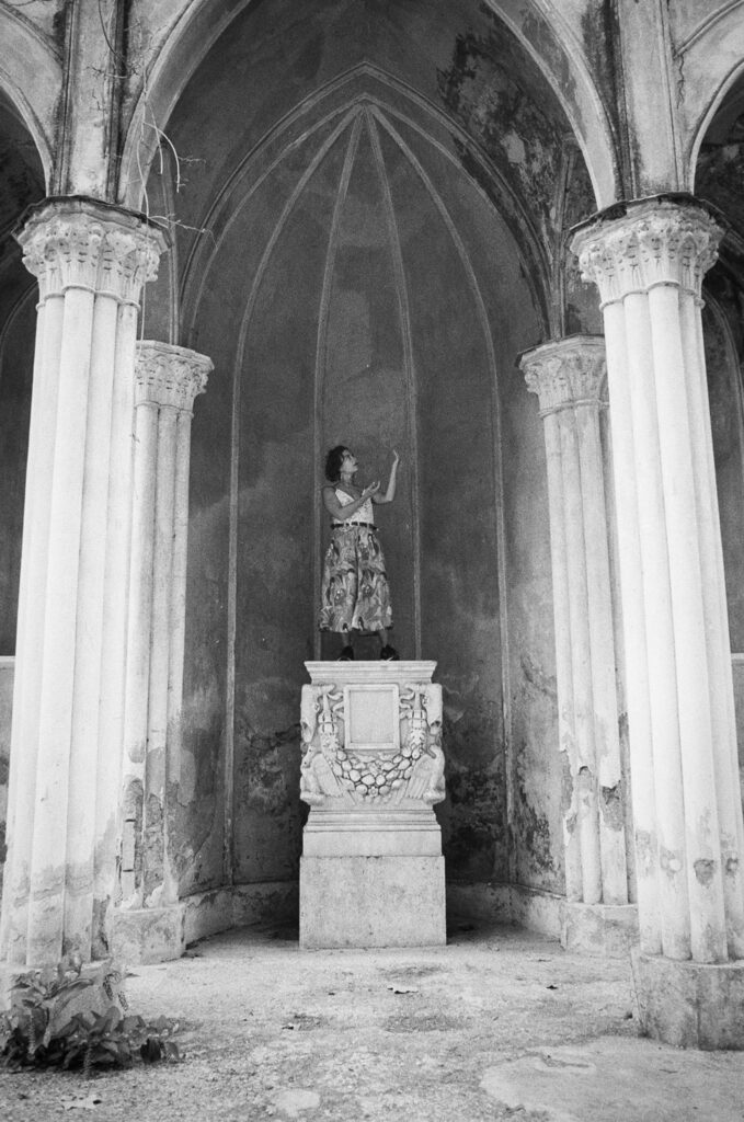 A woman standing on a plinth, inside a vaulted arch.