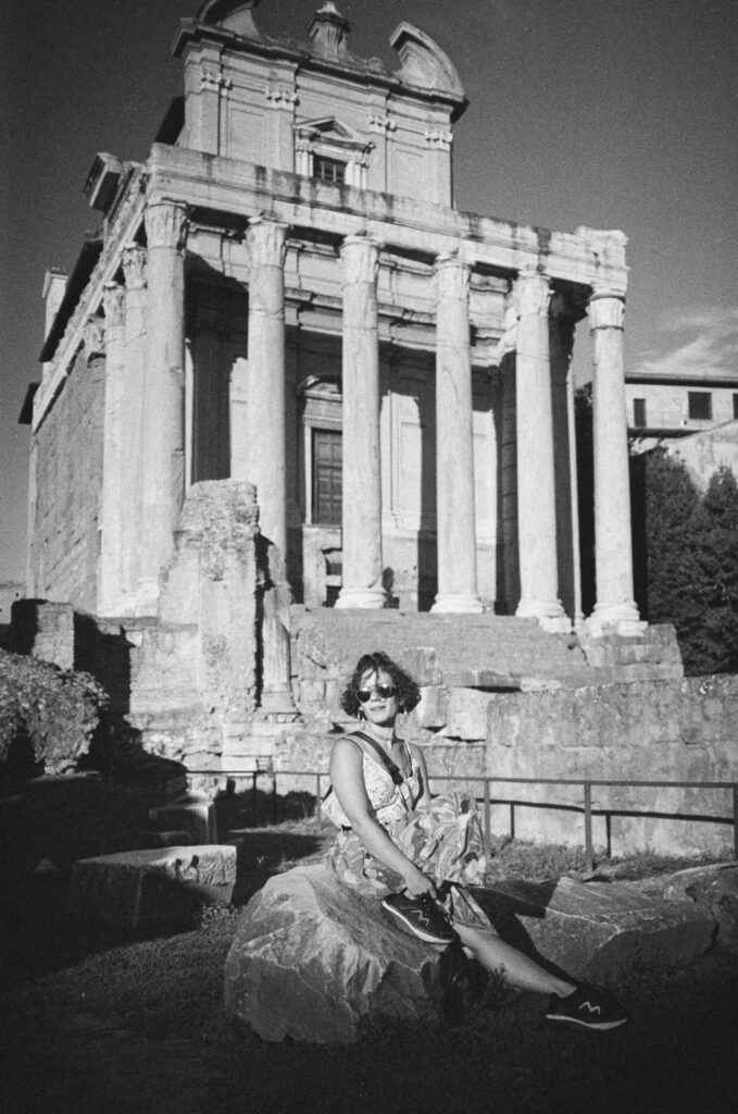a woman sitting in front of the ruin of a roman temple