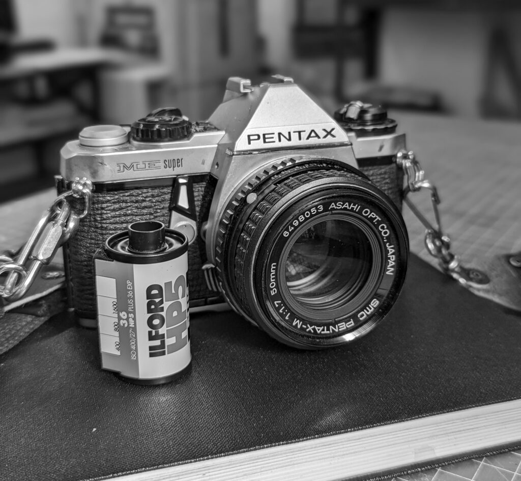 a Pentax camera with a roll of HP5+, sitting on a notebook