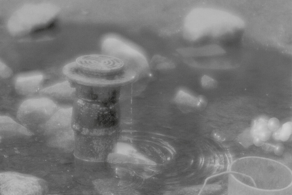 Drainpipe in a pool of water, surrounded by rocks.