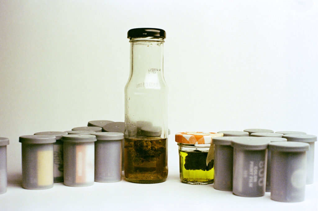 Two small glass containers with green liquid surrounded by 20 rolls of 135 film