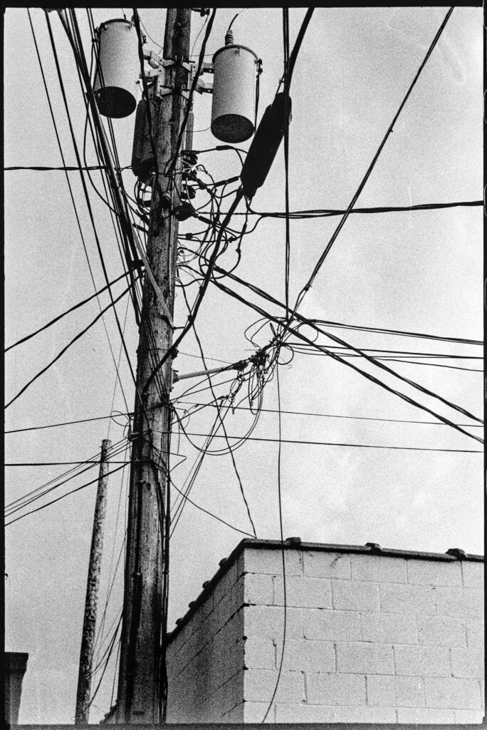 Electrical wires and transformers on a pole. Moody sky in the background. The wires bisect the photo in many ways.