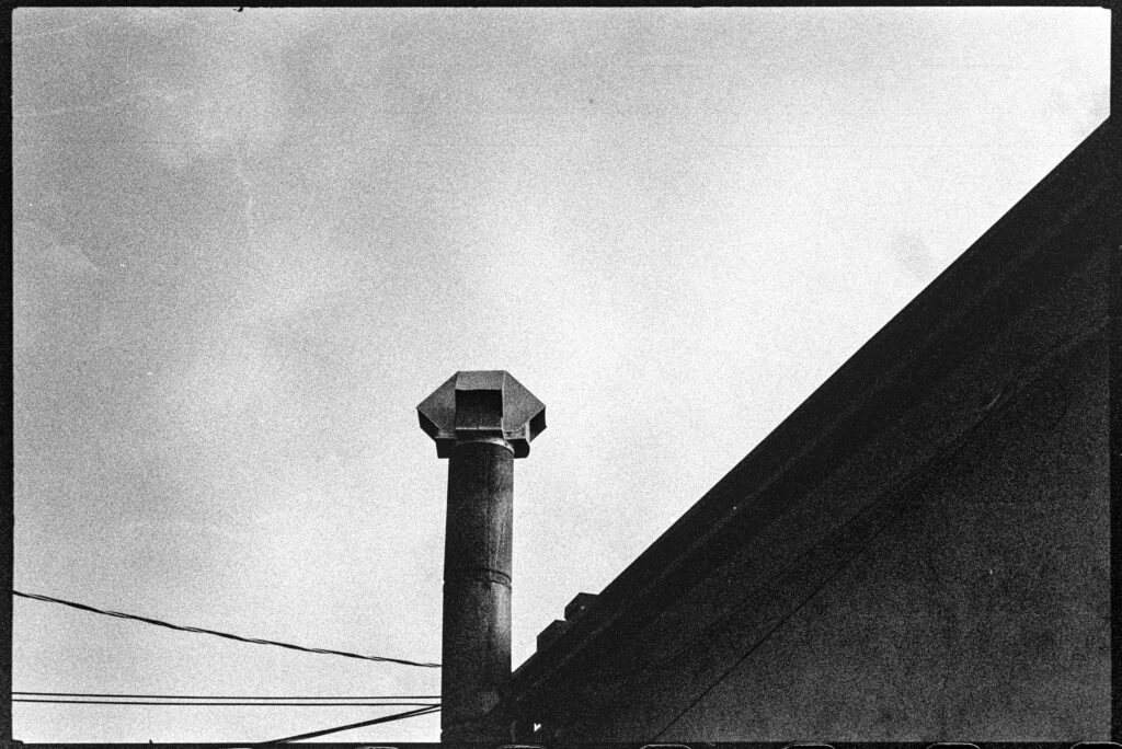 A building with an exhaust pipe sticking up. Dramatic clouds are in the background.