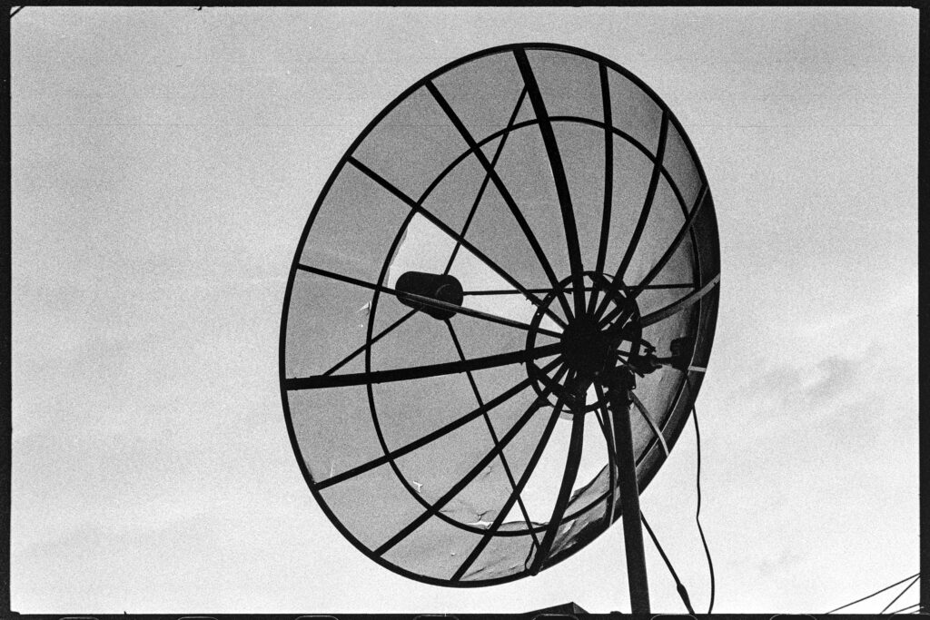 A damaged satellite dish with a cloudy sky in the background.