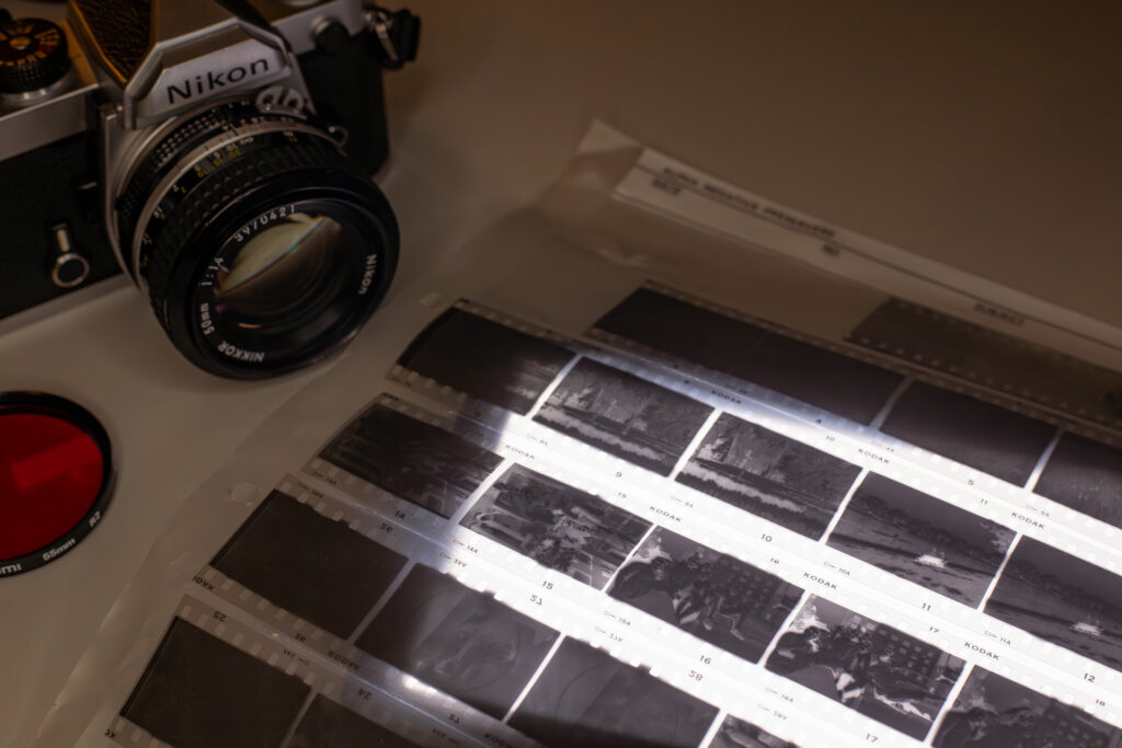 Photograph of a 35mm negative sheet filled with Kodak High Speed Infrared (HIE) negatives over a light table, with a Nikon FM film camera and deep red lens filter to the side.