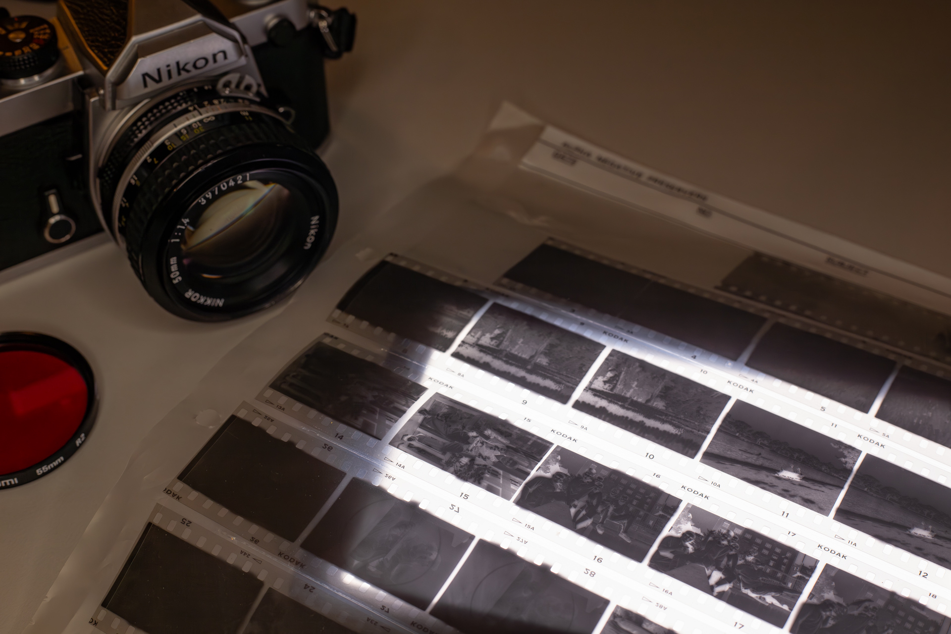 Photograph of a 35mm negative sheet filled with Kodak High Speed Infrared (HIE) negatives over a light table, with a Nikon FM film camera and deep red lens filter to the side.