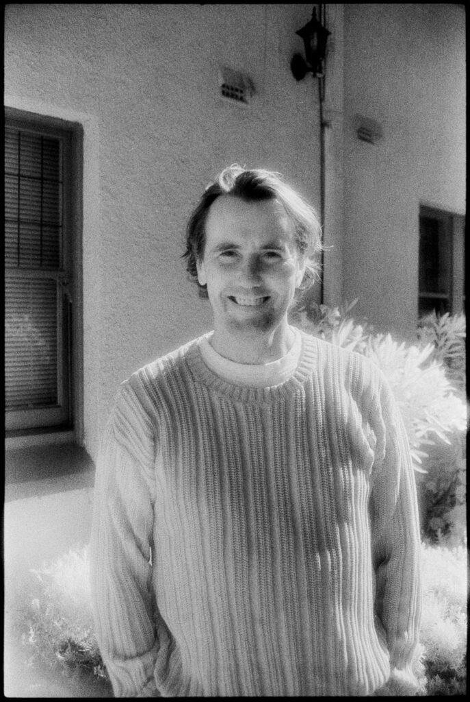 Black and white infrared photograph of a man smiling in front of a building