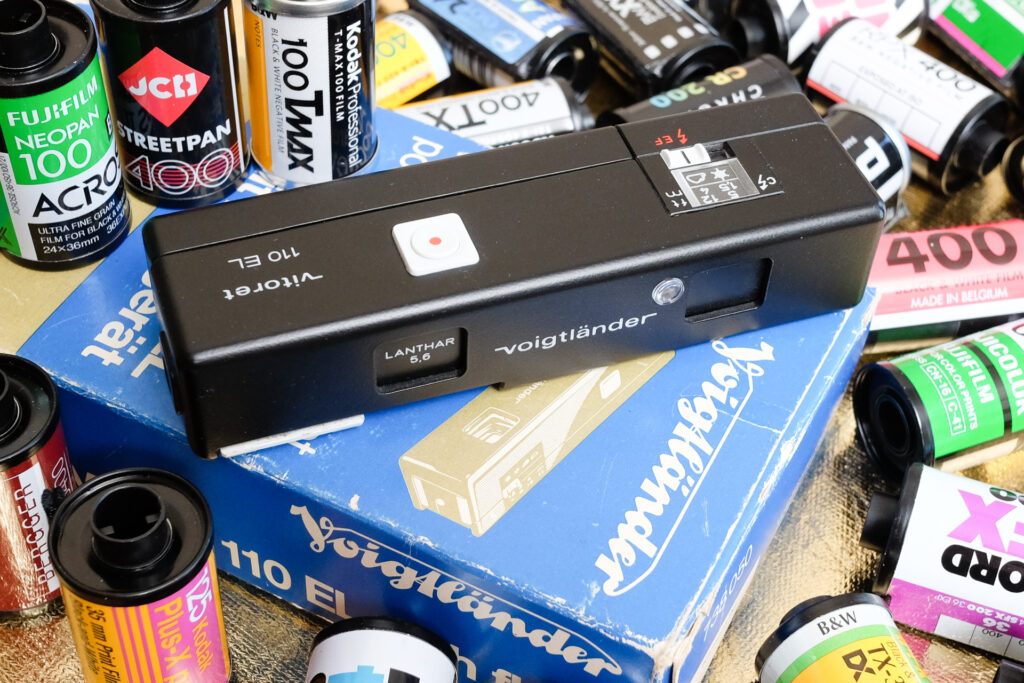 Voigtlander Vitoret 110 EL camera on top of its box surronded by 35mm film canisters